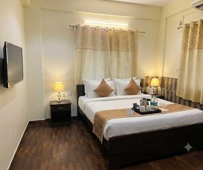 A hotel room with a bed, bedside lamps, a flat-screen TV, a tray with toiletries, and a mirror. - Deluxe City Place Kolkata (Barasat)
