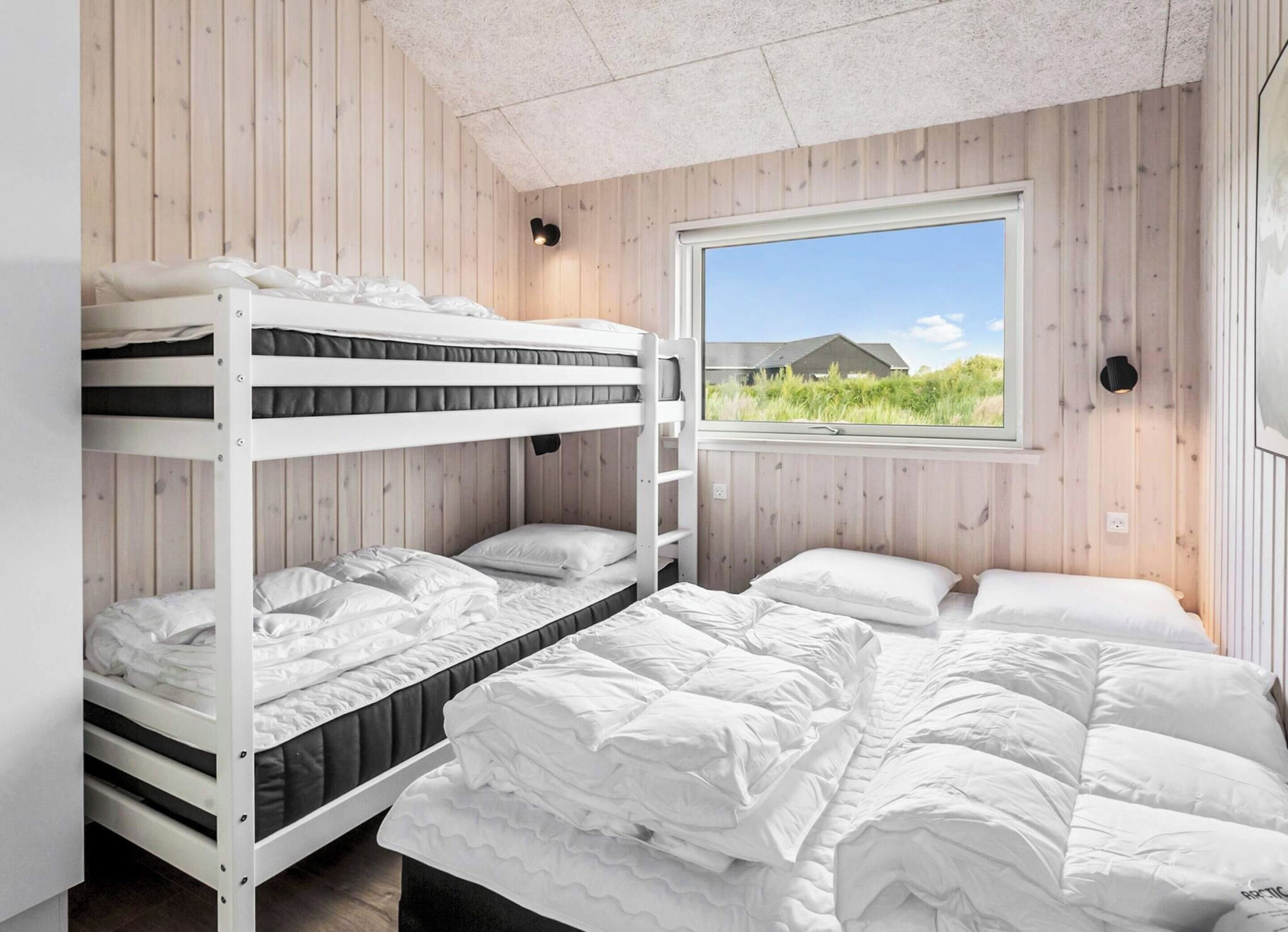 A bunk bed room with a window view of greenery and a house.