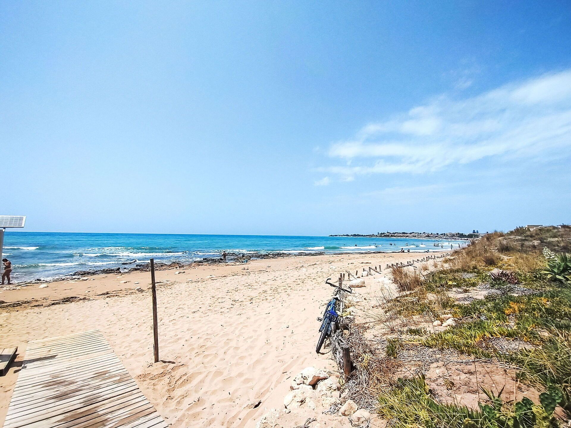Une plage avec une promenade en bois menant à la mer, un vélo garé sur le sable et un ciel dégagé.
