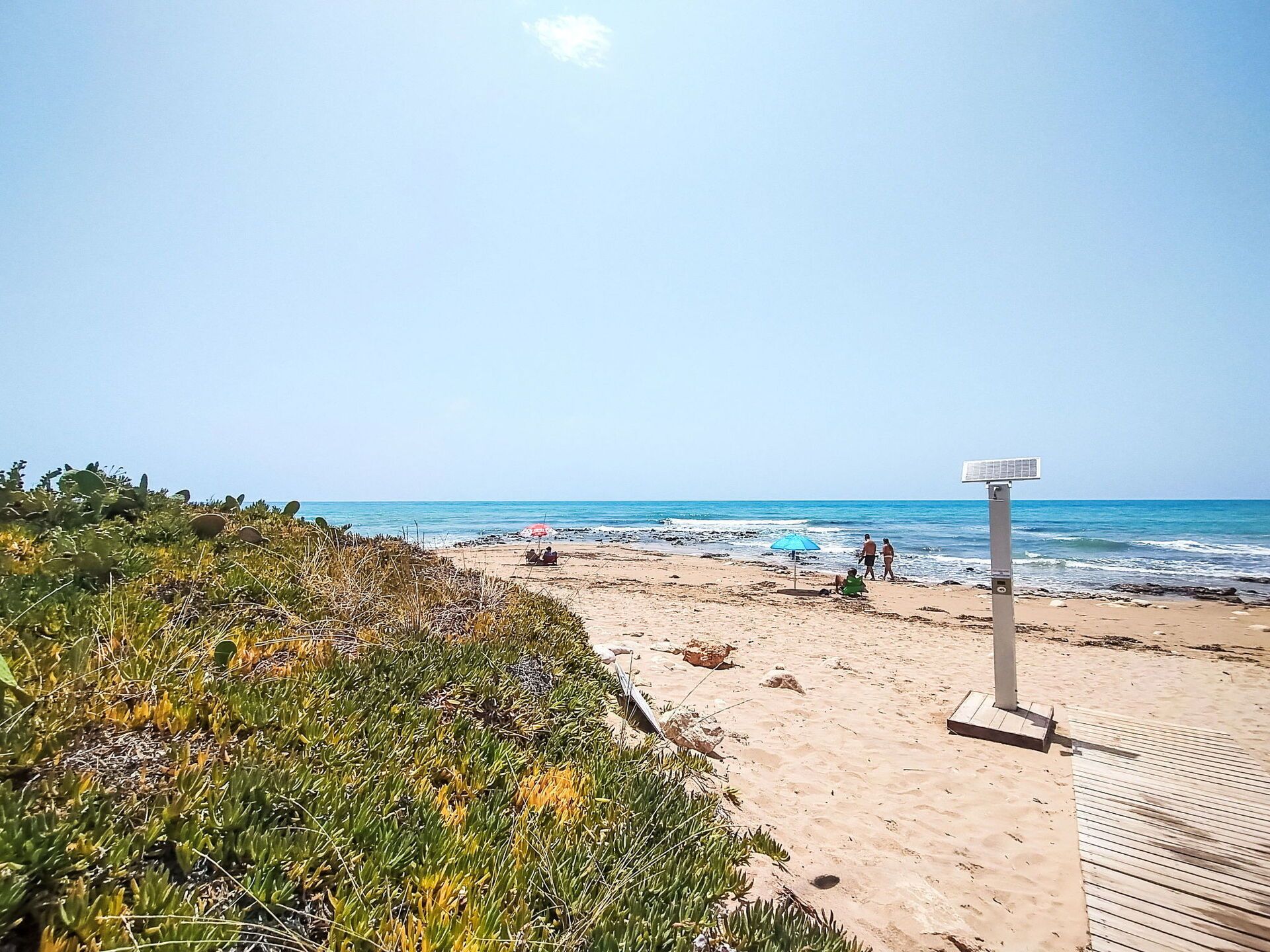 Ein Strand mit einer Holzpromenade, einem Wegweiser und Personen in der Ferne.