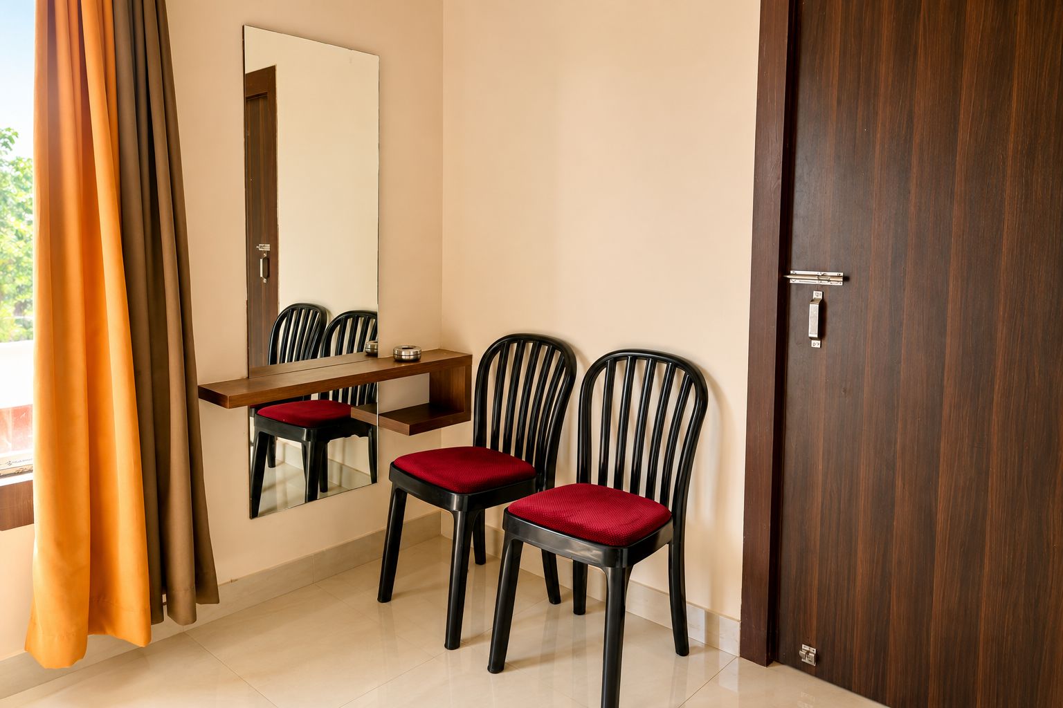 A room with a wooden desk, two chairs with red cushions, a mirror, and a door.
