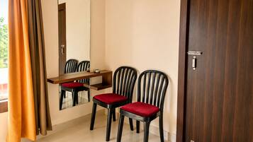 A room with a wooden desk, two chairs with red cushions, a mirror, and a door.