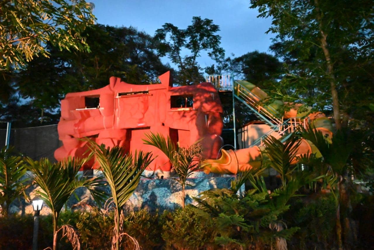 A large red sculpture with a staircase leading up to it, surrounded by tropical vegetation.