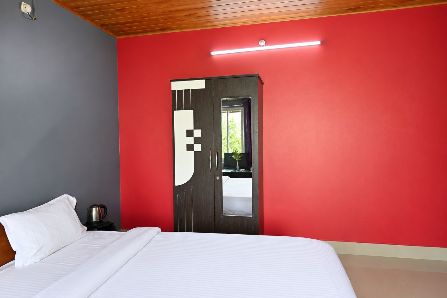 A bedroom with a bed, a nightstand, a coffee maker, and a door with a mirror.