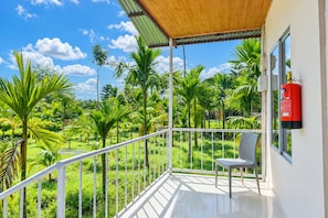 A balcony with a view of a lush garden, a fire extinguisher mounted on the wall, and a chair.