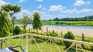 Vista al río desde un balcón con baranda de metal, un área verde y árboles.
