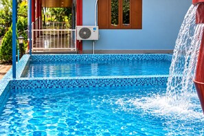 Una piscina con borde de azulejos, una fuente de agua y una zona cubierta con barandilla roja.