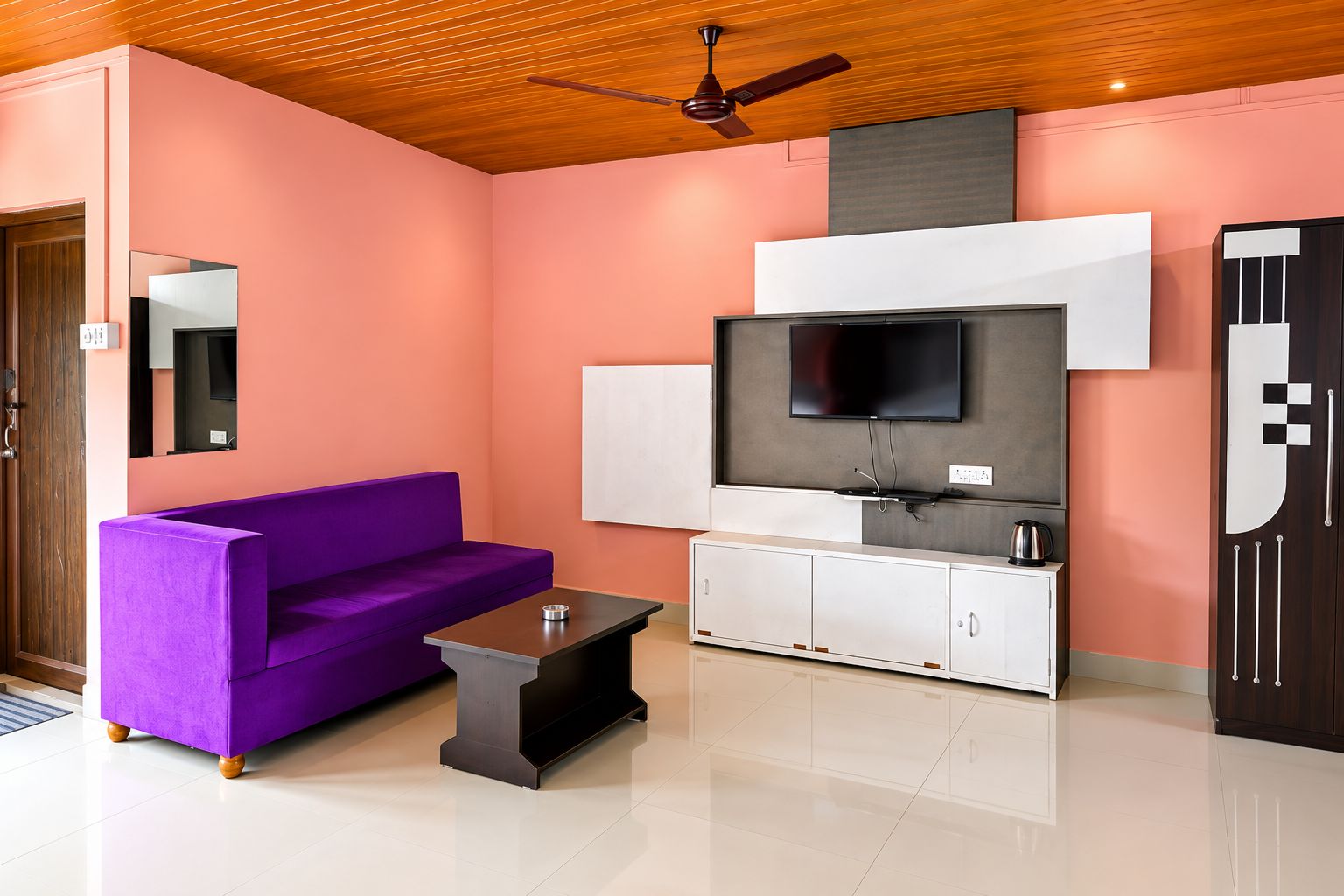Una sala de estar moderna con un sofá púrpura, una mesa de centro, un televisor de pantalla plana y un ventilador de techo.