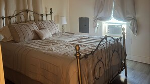 Une chambre à coucher comprenant un lit, un ventilateur de plafond, une fenêtre avec des rideaux et un radiateur fixé au mur.