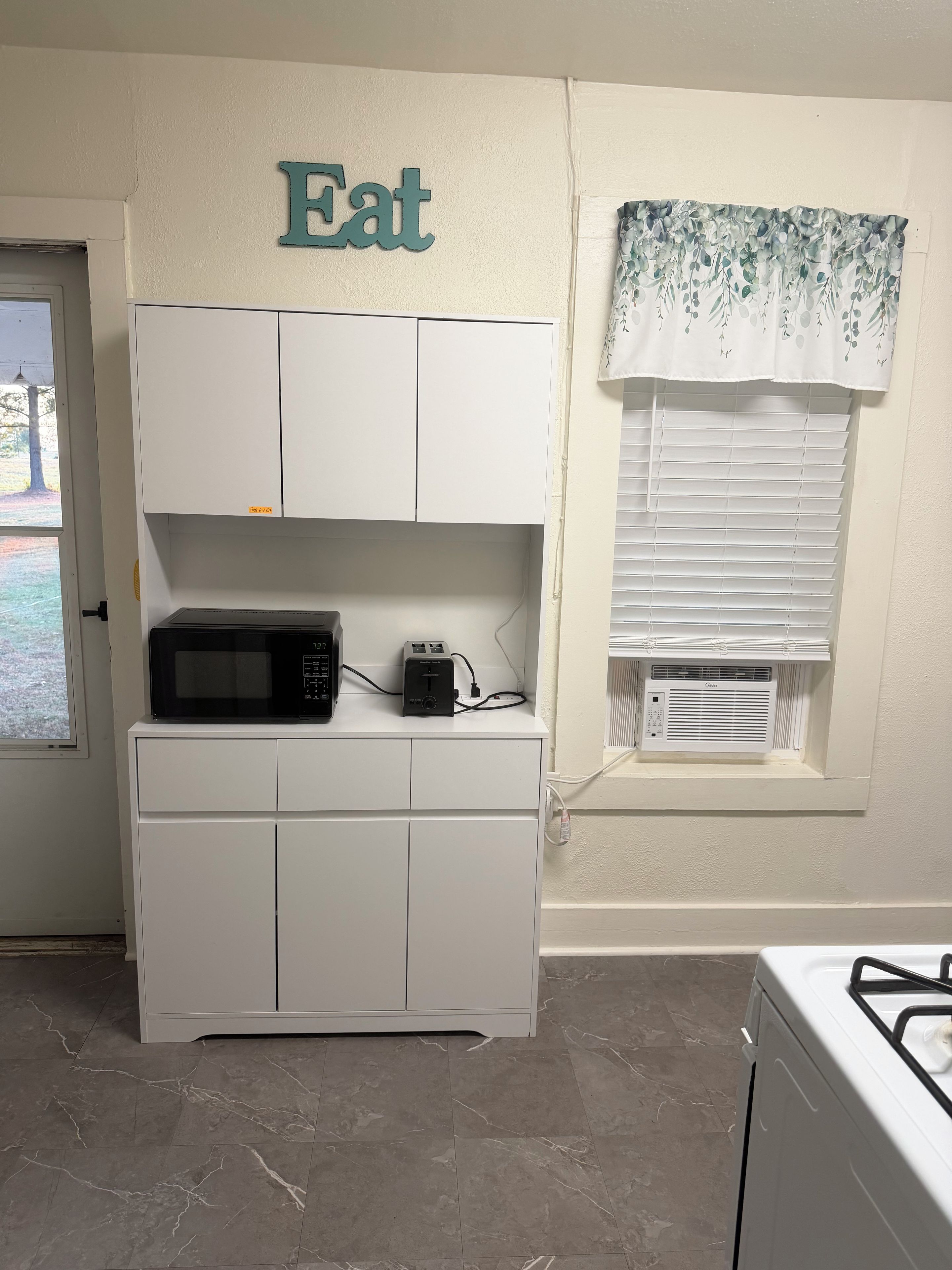 A kitchen with white cabinets, a microwave, a toaster, and a window with blinds.