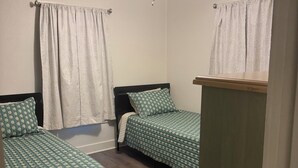 Une chambre avec deux lits simples, un ventilateur de plafond et un plancher en bois.
