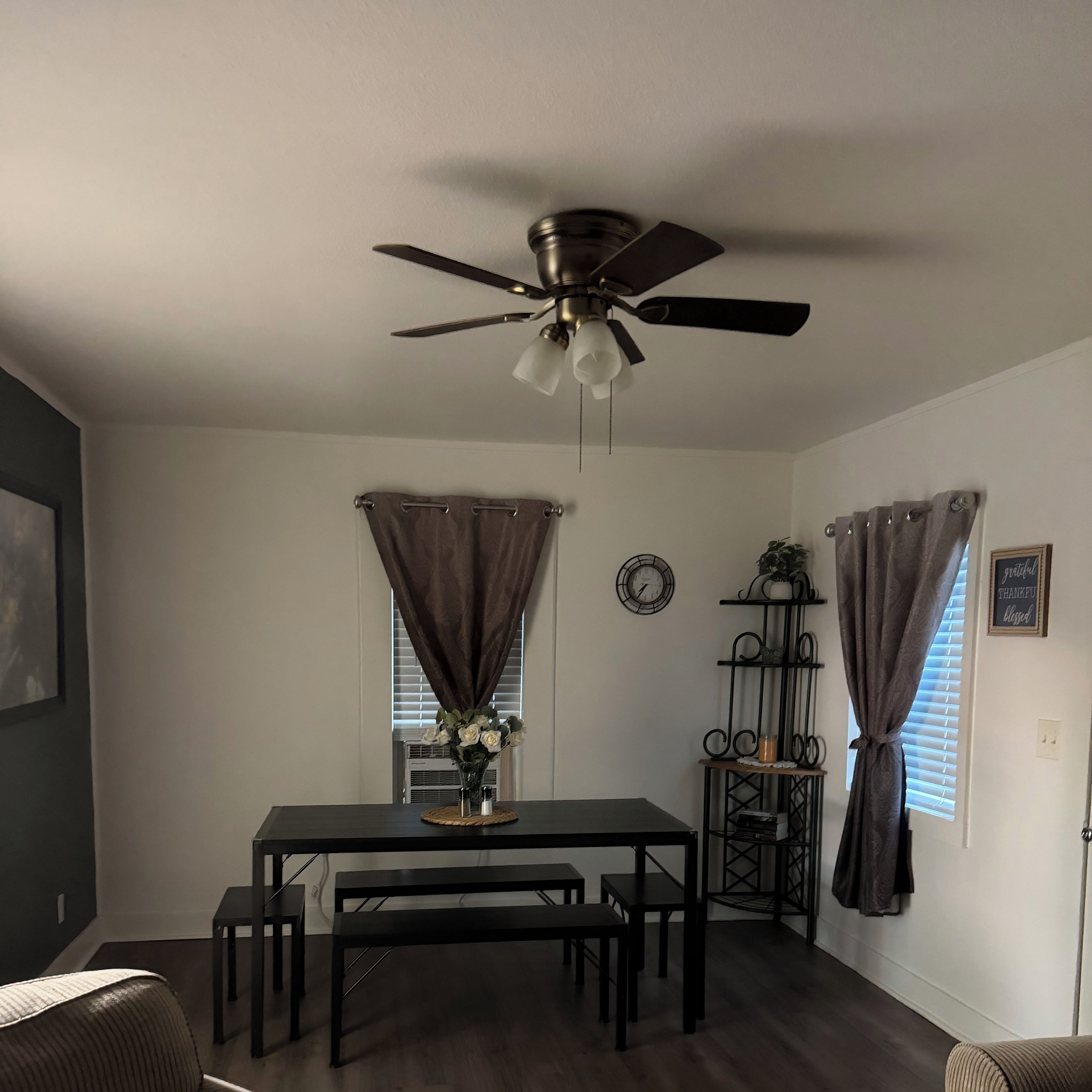 A dining area with a table and benches, a ceiling fan, and a wall clock.