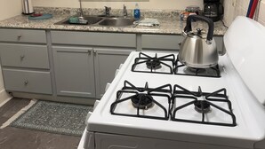 Une cuisine équipée d’une cuisinière à gaz, d’une machine à café et d’une fenêtre avec des stores.