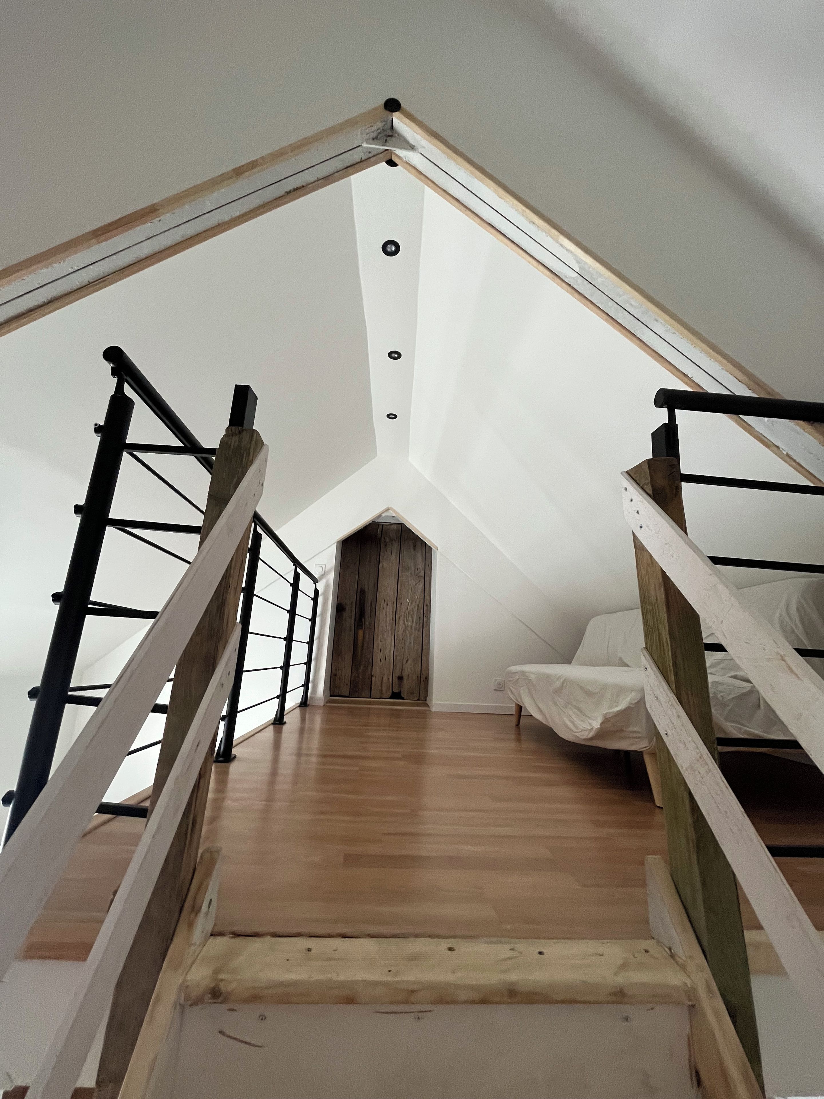 Un dormitorio tipo loft con piso de madera, techo inclinado y cama con cubierta blanca.