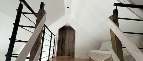 Un dormitorio tipo loft con piso de madera, techo inclinado y cama con cubierta blanca.