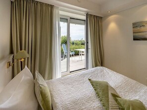 Quarto de hotel com cama, cortinas, luminária e vista para o exterior.
