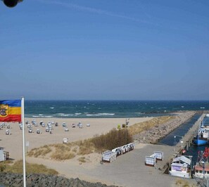 Ein Strand mit Reihen von Liegestühlen und Sonnenschirmen, eine Fahnenmast mit einer Flagge und ein Steg mit Booten.