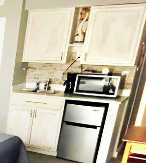 A compact kitchen with white cabinets, a microwave, and a refrigerator. - Pool Tiki Bar Oceanview Studio w/kitchenette (Daytona Beach)