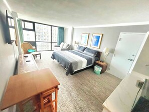 Une chambre d’hôtel comprenant un lit, un bureau, une chaise, une armoire et une fenêtre donnant sur des immeubles.
