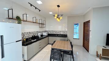 Cozinha moderna com geladeira, micro-ondas e fogão. Há uma mesa de jantar com cadeiras e uma luminária pendente.