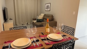 Mesa de jantar posta com pratos, talheres e copos de vinho, com uma garrafa de vinho e um controle remoto sobre a mesa.