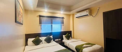 A hotel room with two beds, a ceiling fan, an air conditioning unit, and a window with blinds.