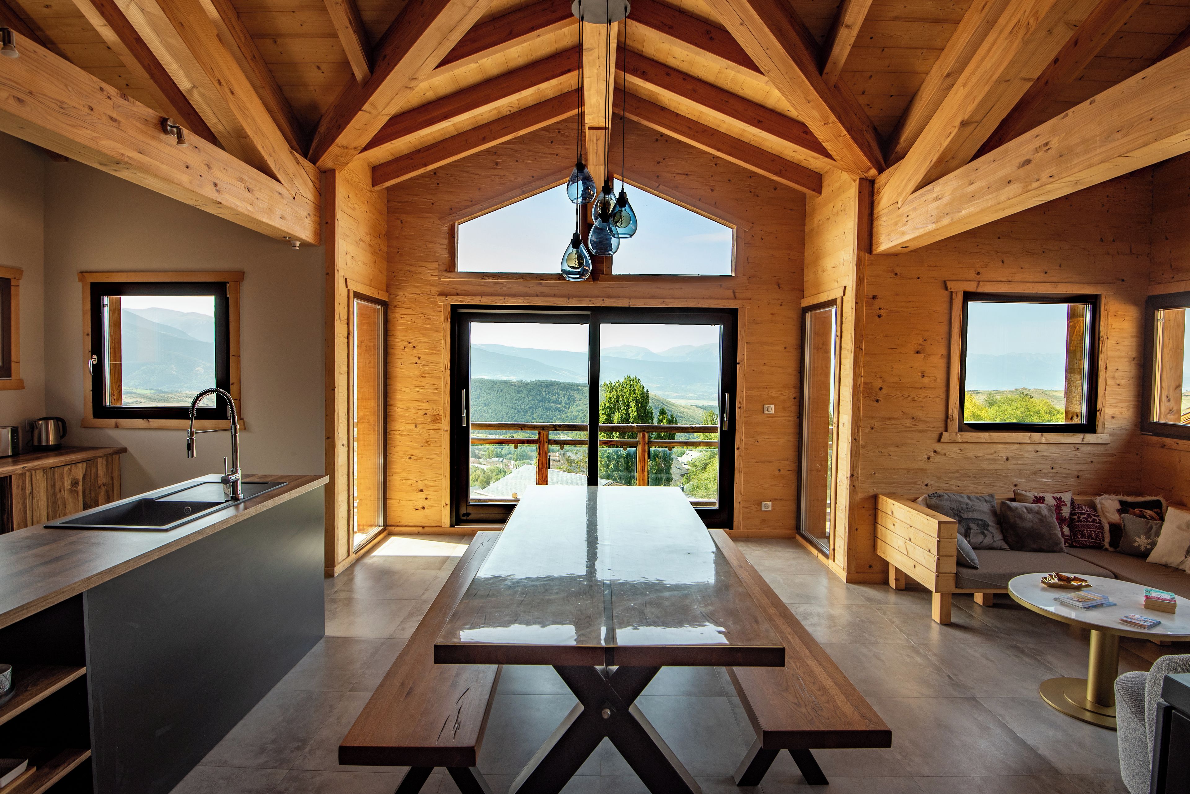 A modern kitchen with a large island, wooden beams, and a view of mountains through the windows.
