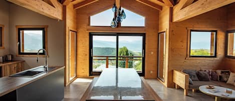 A modern kitchen with a large island, wooden beams, and a view of mountains through the windows.