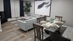 A modern dining area with a grey sofa, wooden dining table, and chairs. - 6 Beds Ideal for Crews & Insurance I Close to Naval Base and 6 flags (Waukegan)