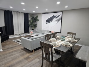 A modern dining area with a grey sofa, wooden dining table, and chairs. - 6 Beds Ideal for Crews & Insurance I Close to Naval Base and 6 flags (Waukegan)