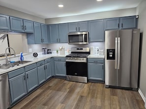 A modern kitchen with grey cabinets, stainless steel appliances, and a wooden floor.