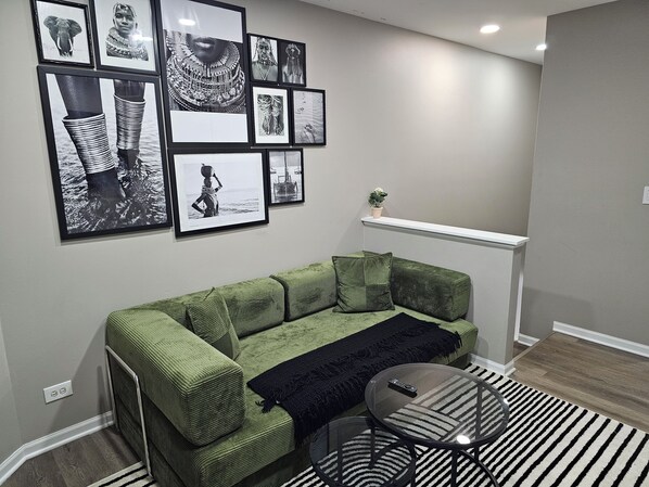 A living room with a green sofa, a glass coffee table, and a black and white striped rug.