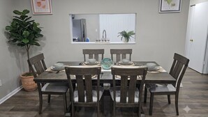 A dining area with a table set for six, surrounded by chairs, a potted plant, and framed artwork on the walls. - 6 Beds Ideal for Crews & Insurance I Close to Naval Base and 6 flags (Waukegan)