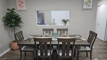 A dining area with a table set for six, surrounded by chairs, a potted plant, and framed artwork on the walls.