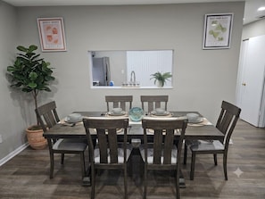 A dining area with a table set for six, surrounded by chairs, a potted plant, and framed artwork on the walls. - 6 Beds Ideal for Crews & Insurance I Close to Naval Base and 6 flags (Waukegan)
