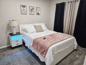 A bedroom with a bed, bedside table, lamp, and wall art.