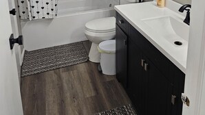 A bathroom with a bathtub, toilet, and a sink with a mirror. - 6 Beds Ideal for Crews & Insurance I Close to Naval Base and 6 flags (Waukegan)