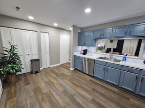 A modern kitchen with wooden flooring, grey cabinets, and stainless steel appliances.