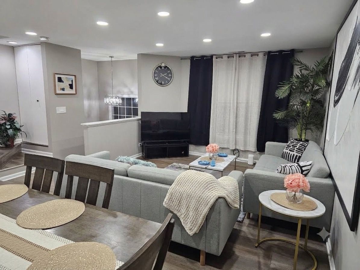 A modern living room with a sofa set, a dining table with placemats, a coffee table, and a television.
