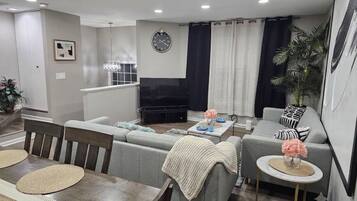 A modern living room with a sofa set, a dining table with placemats, a coffee table, and a television.