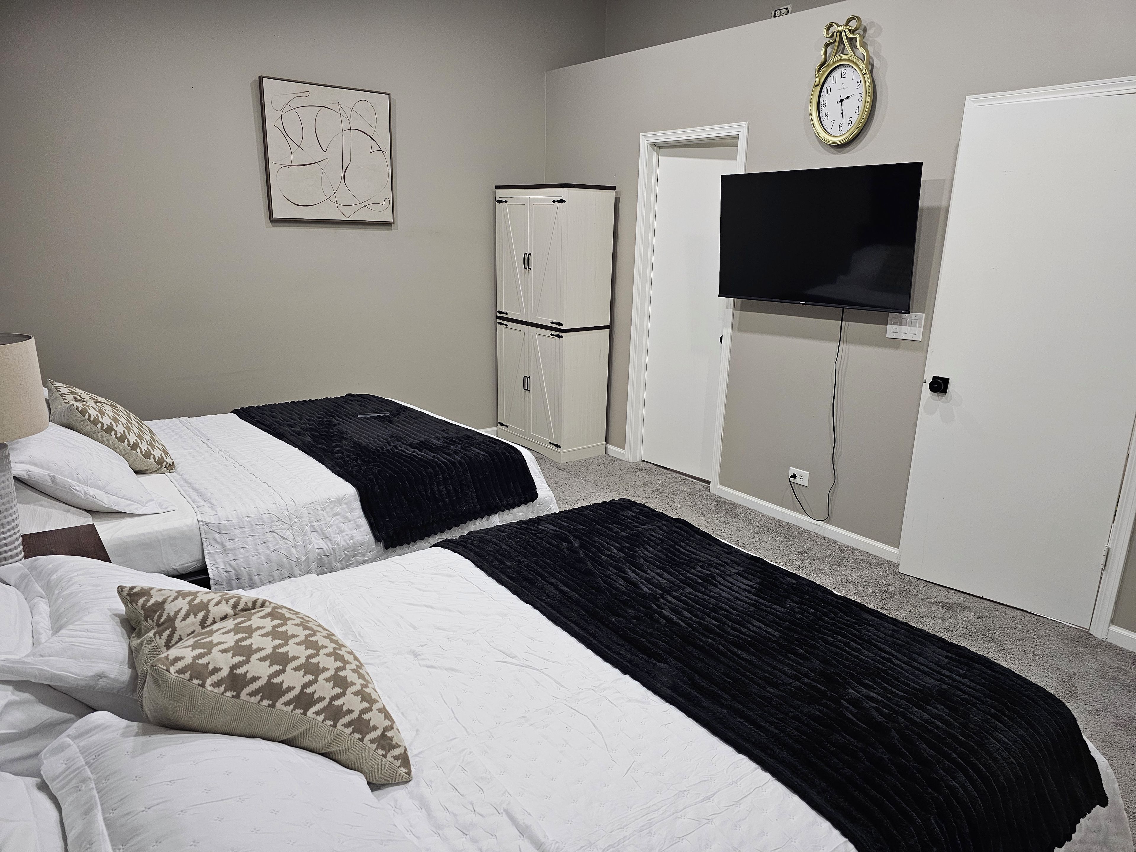 A bedroom with two beds, a wardrobe, a television, and a clock on the wall.