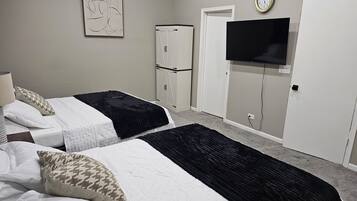 A bedroom with two beds, a wardrobe, a television, and a clock on the wall.