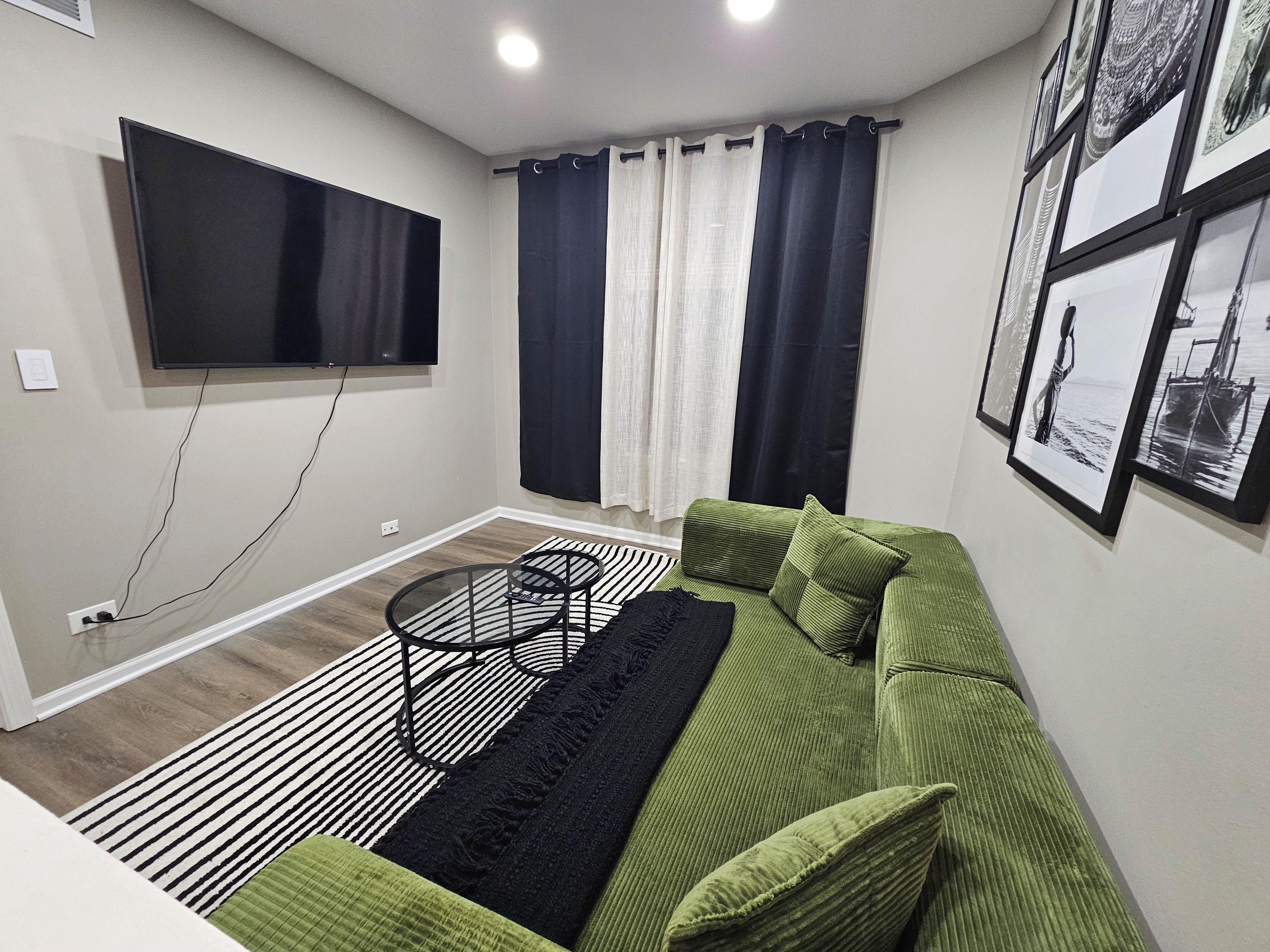 Ein Wohnzimmer mit einem grünen Sofa, einem schwarzen Couchtisch, einem flachbildfernseher an der Wand und einem Fenster mit Vorhängen.
