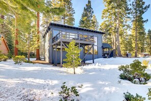 Eine Holzhütte mit einer Terrasse, umgeben von hohen Bäumen und Schnee.