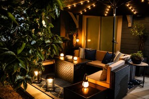 An outdoor seating area with a sofa, table, and lanterns, surrounded by greenery and string lights. - Lux Pacific Beach - Rooftop Terrace, Walk to Sand (San Diego)