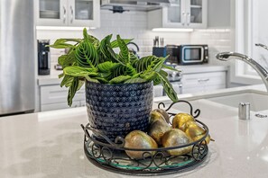 Un taulell de cuina amb un ram blau decoratiu, fulles verdes i un bol metàl·lic amb fruites daurades.