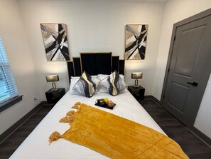 A hotel room with a bed, two bedside tables, a door, and abstract artwork on the walls. - The Luxury Den Just Mins from Downtown Houston (Houston)