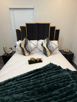 Ein Bett mit schwarzem Kopfteil, zwei Zierkissen, einer grünen Decke und einem Nachttisch mit einem Dekorationsobjekt.
