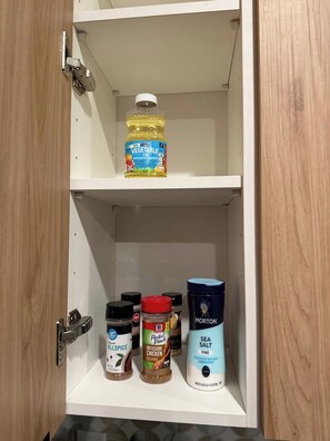 Een keukenkastje met een fles plantaardige olie, een potje kruidnagel, een bakje Perfect Pinche kruiden en een verpakking Morton Zeezout.