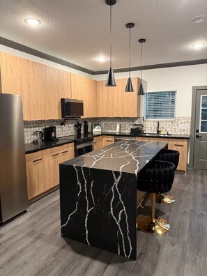 A modern kitchen with wooden cabinets, a black marble island, and pendant lighting. - The Luxury Den Just Mins from Downtown Houston (Houston)